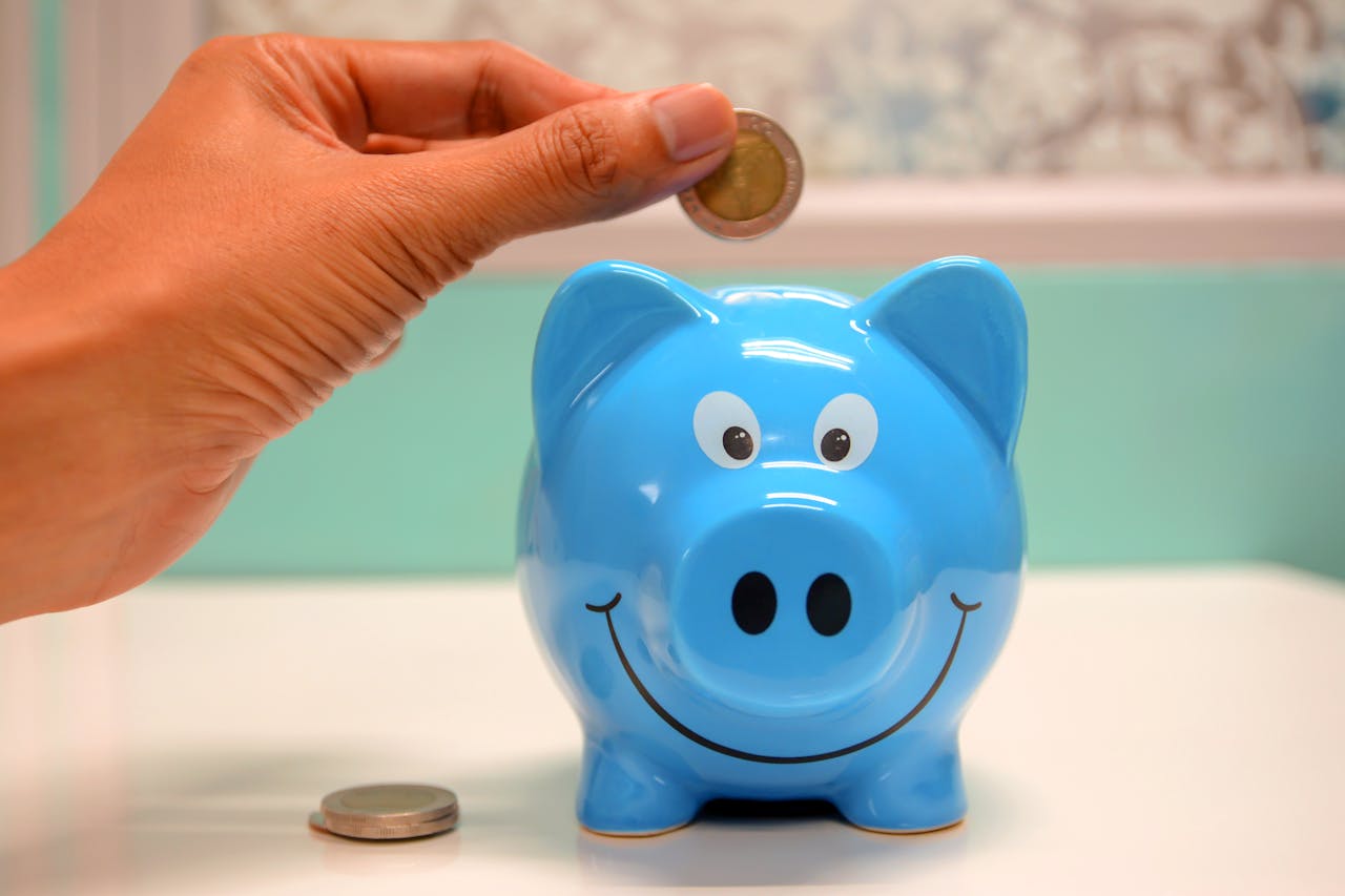 who-we-are Hand inserting a coin into a blue piggy bank for savings and money management.