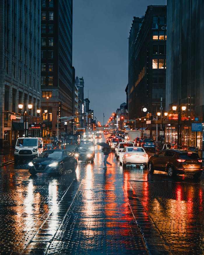 A vibrant night scene of urban traffic with illuminated city buildings and reflections on wet streets.